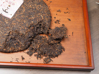 Pried pieces of Dayi 7572 ripe puerh tea cake on a wooden tea tray, ready for brewing.
