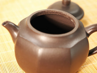 Close-up of open mouth of Shihuang Bafang Yixing teapot showing rim thickness and interior, lid blurred behind