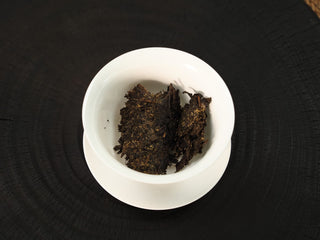 Chunks of The Little Brick 2018 fu brick tea with visible golden flowers placed in a white porcelain gaiwan before brewing