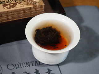 The Yunnan Mini Ripe Pu-erh Tea Brick unfolding in a gaiwan, revealing rich reddish-brown tea liquor and smooth shou Pu-erh infusion.