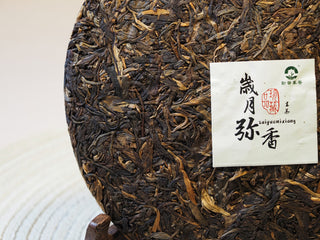 Surface detail of the 2005 Lincang vintage raw Pu-erh tea cake displaying natural oil sheen and leaf variation.