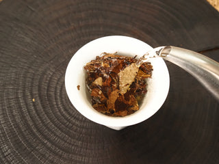 Hot water poured from a metal kettle into the gaiwan of 2013 Fuding Shou Mei leaves, the first rinse awakening the aged leaf.