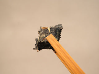 Section of 2014 Fuding Shou Mei waffle cake held with bamboo tongs, showing broad aged leaves and stems broken from the cake.