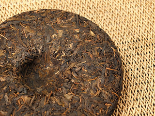 Close-up of the center dimple on Jing Chang Hao Quiet Years 2018 raw Pu-erh cake, loose twisted Bulang arbor leaves around the nest