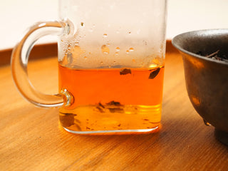 Close-up of the deep amber-orange tea liquor from 2018 sun-dried Fuding White Peony compressed tea biscuit, brewed in a clear glass mug.