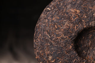 Side view of the 2019 Bojun 500g cake, showing the tightly pressed dark fermented leaves with golden tips on a dark background.