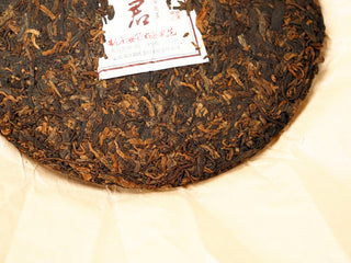 Lower-half detail of the 2020 Bojun 500g cake, showing the inner ticket and pressed dark fermented leaves with golden buds.