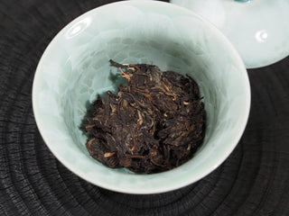 Pried loose tea leaves of 2021 Dayi Guanchao Raw Puerh Tea inside a celadon gaiwan bowl ready for brewing.
