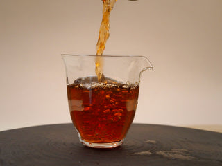Pouring deep red liquor of 2024 Bulang Mountain ripe pu-erh into a glass pitcher