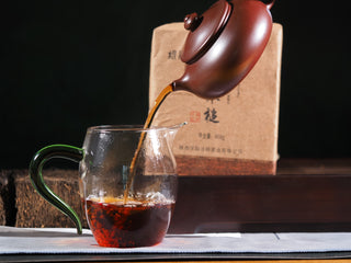 Pouring the rich, dark amber tea liquor of the 2019 aged Hei Cha into a clear glass pitcher.
