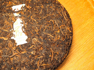 Side view of the Bojun Ripe Pu-erh 7.0 500g cake with the inner ticket visible at center, pressed leaf structure clear.