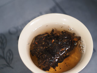 Initial infusion of the 2013 aged Fu Brick tea in a white porcelain cup, showing the awakening of the dark tea leaves.

