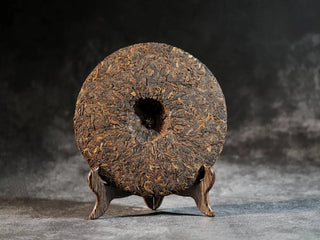 Back view of unwrapped Bulang Mountain Ancient Tree Ripe Pu-erh tea cake, showing compressed tea structure and dark glossy leaves