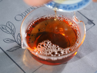 Rich and vibrant orange-red liquor of the brewed Fu Brick dark tea with natural bubbles in a glass pitcher.
