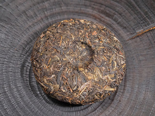 The back side of the pressed Dayi 7542 raw puerh cake showing the traditional indentation and dark tea leaves.