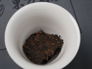 Loose dry leaves of 2022 Dayi 7572 ripe puerh tea inside a white porcelain gaiwan before brewing.
