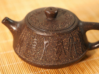 Close-up of the Guyun Shipiao Yixing teapot lid with embossed scroll motifs above the carved sandy clay body