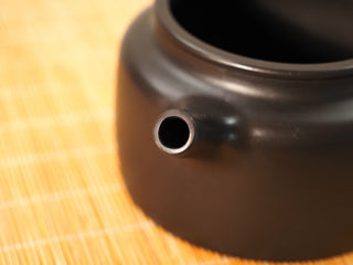 Close-up of the straight spout opening of a Heini Dezhong Yixing teapot, dense black clay body on a bamboo mat