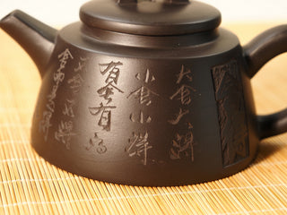 Close-up of engraved Chinese calligraphy characters on the Black Zhu Ni Shede Yixing teapot body, bamboo mat behind