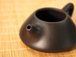 Close-up of the spout opening of a Black Zhu Ni Ziye Shipiao Yixing teapot, dark smooth clay body on a bamboo mat