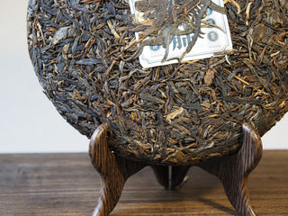 Mangfei Mountain raw Pu-erh tea cake displayed on a wooden stand