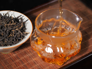 Pouring brewed Ancient Tree Dianhong black tea into glass pitcher