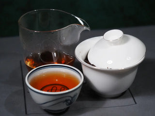 Premium Wuyi Yancha Huang Guan Yin tea tasting set featuring a cup of tea, glass pitcher, and porcelain gaiwan.