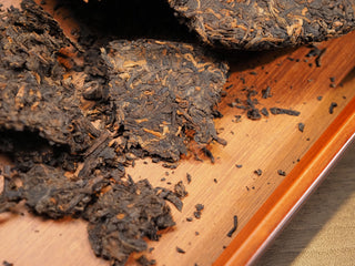 Pried loose tea leaves of 2021 Dayi 7572 ripe puerh cake on a wooden tea tray, ready for brewing.