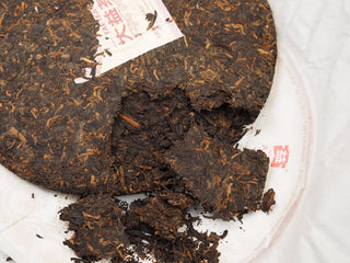 Pried open chunks and loose tea leaves of 2019 Dayi 7572 ripe puerh cake on its wrapper paper, ready for brewing.