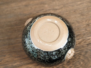 Base of a Rui Shou sky eye oil spot Jianzhan bowl placed upside down, showing the unglazed foot ring with a small impressed makers mark and two raised clay medallions on the body.