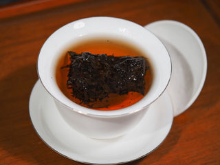 Aged dark tea leaves steeping to release a rich amber-colored liquor.