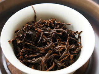 Close-up view of dark, twisted dry leaves of Yunnan Shaken-Leaf Black Tea in a white porcelain cup.
