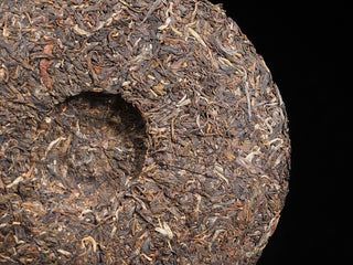 Detailed texture of dry loose tea leaves on the edge of a 2016 Dayi 7532 raw Puerh tea cake, displaying natural aging color.