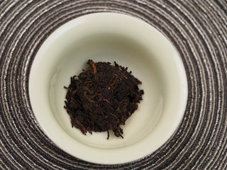Loose dry tea leaves of 2018 Dayi V93 ripe puerh inside a white gaiwan