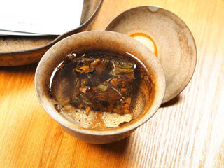2018 sun-dried Fuding White Peony compressed tea biscuit steeping in a ceramic gaiwan, leaves beginning to unfurl in hot water.