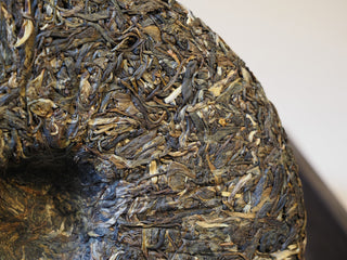 Detailed macro texture of the loose-pressed ancient tree raw puerh tea cake surface.