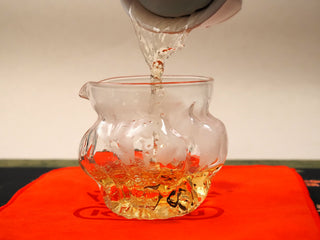 Golden amber tea liquor poured from a gaiwan into a glass fairness pitcher after brewing 2024 Shou Mei and Chen Pi waffle cake.