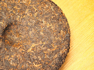Back of the unwrapped Bojun Ripe Pu-erh 7.0 500g cake, showing the tightly compressed dark fermented leaves with golden tips.