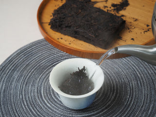 Hot water being poured from a kettle into a white gaiwan to brew the 2013 Dry-Aged Lincang Ripe Pu-erh tea.