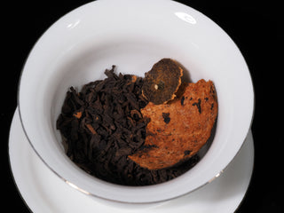 Broken Xinhui citrus peel and Menghai ripe Pu-erh tea leaves placed in a white gaiwan for brewing.