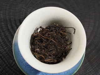 Dry loose leaves of 2020 Dayi 7542 raw puerh tea placed in a white porcelain gaiwan for brewing.
