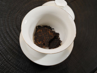 Dry tea leaves of Dayi 7572 ripe puerh tea placed in a white porcelain Gaiwan before rinsing.