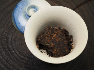 Dry pried leaves of Dayi 7572 ripe puerh tea placed inside a blue-accented white porcelain Gaiwan before rinsing.