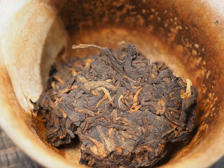 Pried dry tea leaves of Dayi 7452 ripe puerh tea placed in a coarse ceramic brewing vessel before steeping.
