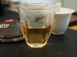 Freshly brewed golden-yellow white tea liquor of Silk Ray Bai Mu Dan inside a clear glass fairness pitcher (Gongdao Bei) next to a gaiwan.