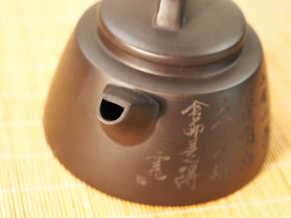 Top-down close-up of the Black Zhu Ni Shede Yixing teapot spout opening, lid and engraved body in soft focus