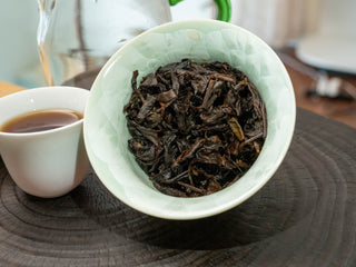 Wet, infused tea leaves (Cha Di) of Mang Fei 2022 loose leaf ripe pu-erh inside a tilted celadon gaiwan.