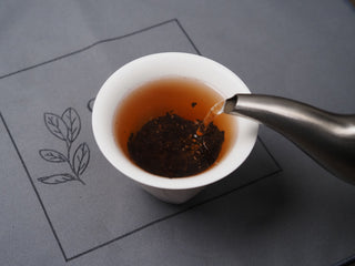 Pouring hot water from a kettle into a white gaiwan with Dayi 7572 ripe puerh tea leaves.
