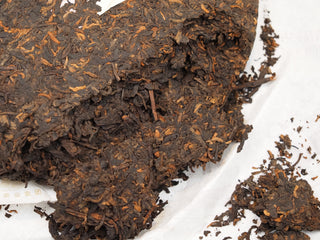 Pried open chunks and loose tea leaves of 2019 Dayi 7592 ripe puerh tea on a white wrapper, ready for brewing.