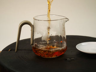 Deep amber-red liquor of The Little Brick 2018 fu brick tea being poured into a clear glass serving pitcher